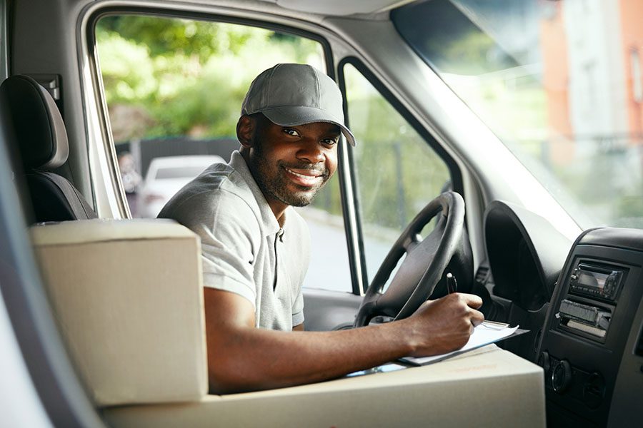 Business Insurance - Portrait of a Smiling Delivery Driver Sitting in a Commercial Van FIlling Out Paperwork