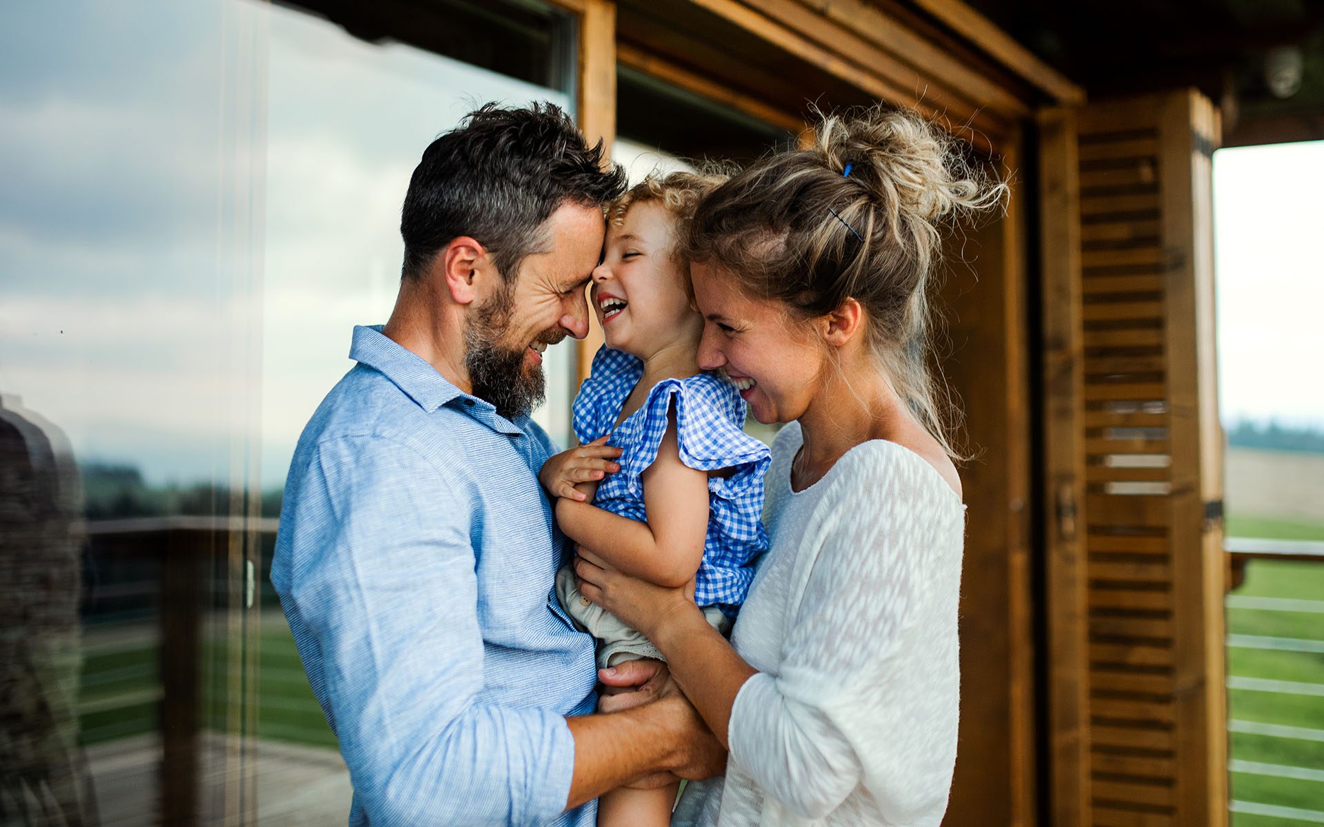 Homepage - Cheerful Family Having Fun Standing Outside on the Front Porch of a Vacation Home in the Countryside